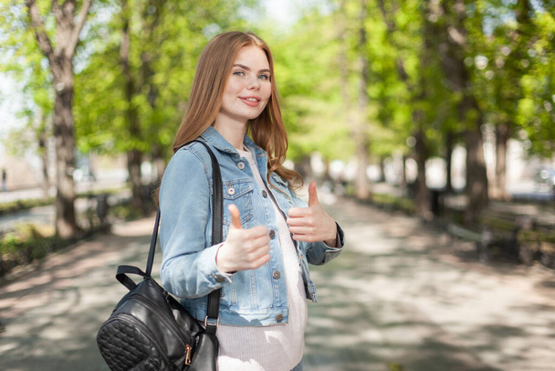 lovely caucasian young woman in denim clothes showing thumbs up in the city - Photo, Image