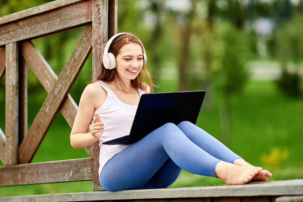 Trabajo remoto de mujer blanca feliz en auriculares con computadora portátil al aire libre. - Foto, Imagen