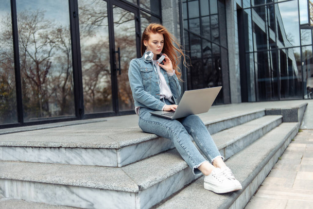 Young woman student or freelancer sits on the stairs with a laptop - Fotoğraf, Görsel
