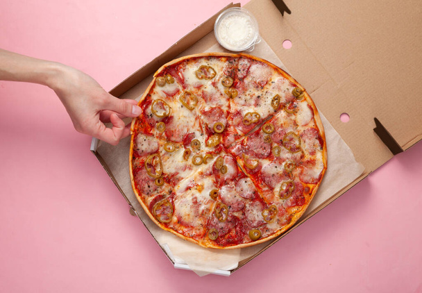Hand neemt een stukje Pizza in open doos op roze achtergrond. Bovenaanzicht - Foto, afbeelding