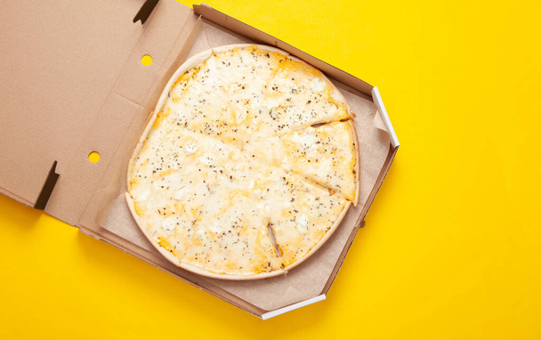 Pizza en una caja abierta sobre fondo amarillo. Vista superior - Foto, Imagen