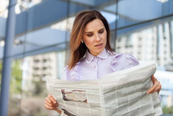 Mujer de negocios sorprendida leyendo un periódico en el fondo del centro de negocios - Foto, imagen