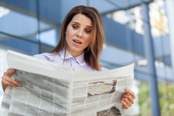 Здивована бізнес-леді читає газету на фоні ділового центру
 - Фото, зображення