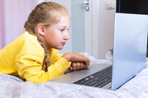 Una adolescente mirando la pantalla de su portátil mientras está acostada en la cama. - Foto, imagen
