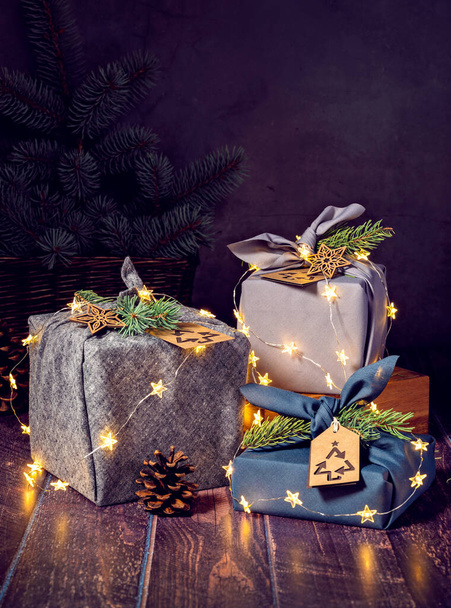Három környezetbarát furoshiki stílusú ajándék csomagolt dobozok sötét háttér fények. Zéró hulladék Karácsony Újrahasznosítás, Fenntartható életmód koncepció. - Fotó, kép