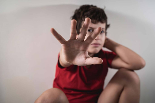 Een kind verstopt zijn gezicht met zijn hand en vraagt om geweld te stoppen. Geen geweld tegen kinderen. - Foto, afbeelding