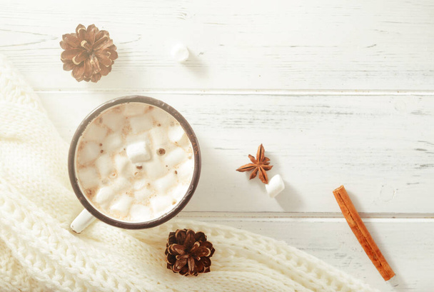 hot chocolate with marshmallows, fir cones, cinnamon sticks, a white sweater on a white wooden background, a place for the inscription, top  view - Φωτογραφία, εικόνα