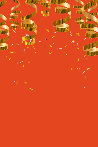 Espirales doradas brillantes, serpentinas y confeti sobre fondo rojo con lugar para texto. Fondo navideño festivo - Foto, imagen