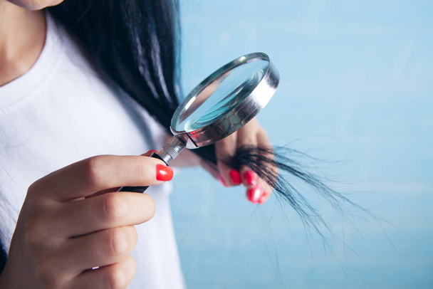 a young girl looks at her hair with a magnifying glass - 写真・画像