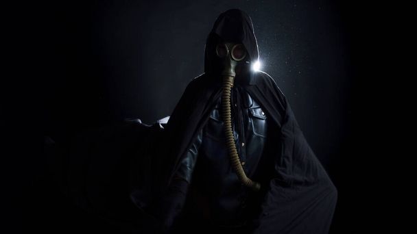 Siyah elbiseli kasvetli bir adam, başında siyah bir başlık, yüzünü koruyan bir gaz maskesi.. - Fotoğraf, Görsel