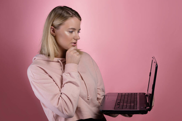 young woman with a laptop, a student or a freelancer. A charming blonde in a pink hoodie - Foto, Imagem