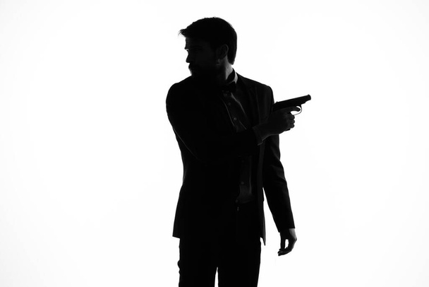 Ο άντρας με το κοστούμι και το πιστόλι στο χέρι, χειρονομία με το χέρι ελαφρό φόντο. - Φωτογραφία, εικόνα