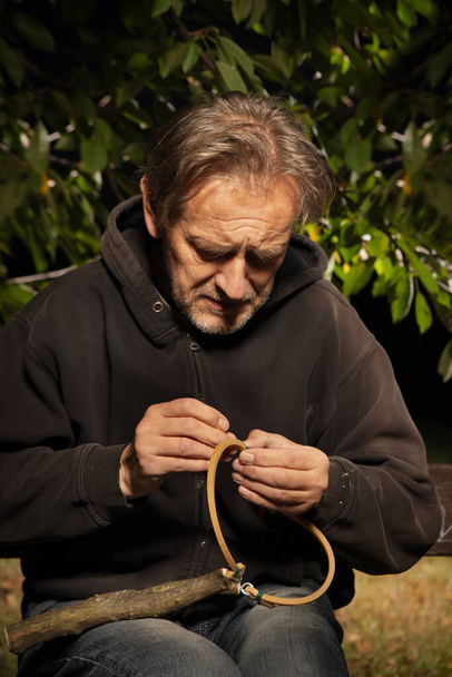 Older man finishing traditional slingshot of wooden fork - Foto, imagen