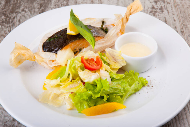 baked trout in paper with salad and white sauce - Foto, Bild