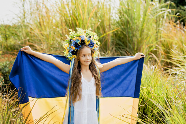 Ukraines Independence Flag Day. Constitution day. Ukrainian child girl in embroidered shirt vyshyvanka with yellow and blue flag of Ukraine in field. flag symbols of Ukraine. Kyiv, Kiev day - Фото, изображение