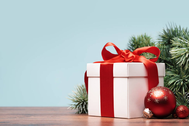 bílá dárková krabice s červenou mašlí stojící v rohu s větví vánočního stromku. Cetky. Vánoční a novoroční hranice. Kopírovat pohled na stranu místa - Fotografie, Obrázek