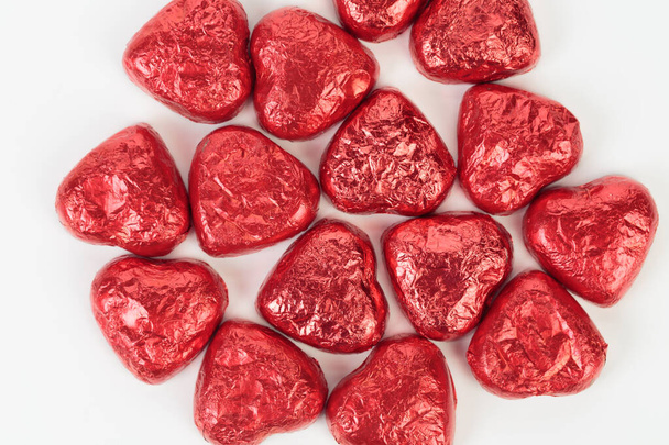 Chocolate heart candies wrapped in red foil. It is located on a white surface. Close-up. - 写真・画像