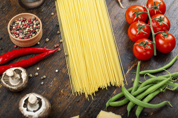 Raw pasta with fresh tomatoes, peppers, asparagus beans, spices and cheese on a wooden table. Food ingredients for Italian spaghetti. - Photo, image