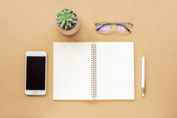 Blank notepad, pen, smartphone, glasses and potted plant on beige table. Top view, flat lay, mock up. - Foto, afbeelding