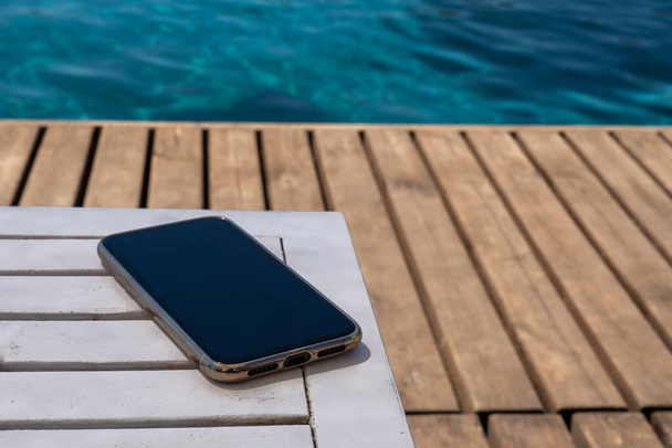 mobilní telefon stojící na dřevěné podlaze u pláže - Fotografie, Obrázek