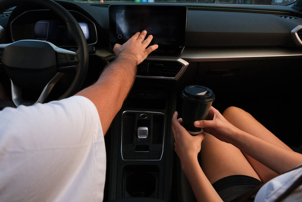 ręka dotykając deski rozdzielczej nawigacji wewnątrz samochodu. Para pijących kawę w samochodzie - Zdjęcie, obraz