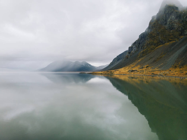 A beautiful scene of a mountain and its reflection in a lake on a foggy day - Photo, Image