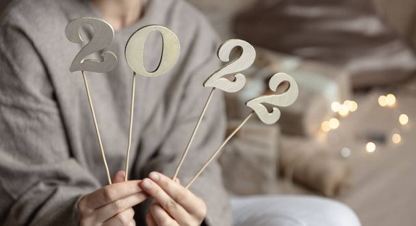 Крупный план деревянных чисел 2022 года на палочках в женских руках на размытом фоне с боке. - Фото, изображение
