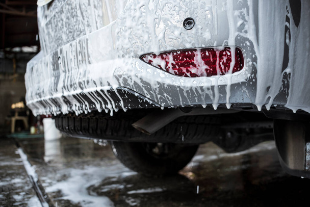 Schuimige shampoo druipt van de achterbumper van een SUV. Tijdens een uitwendige wassen, onderdeel van de auto detaillering service. - Foto, afbeelding