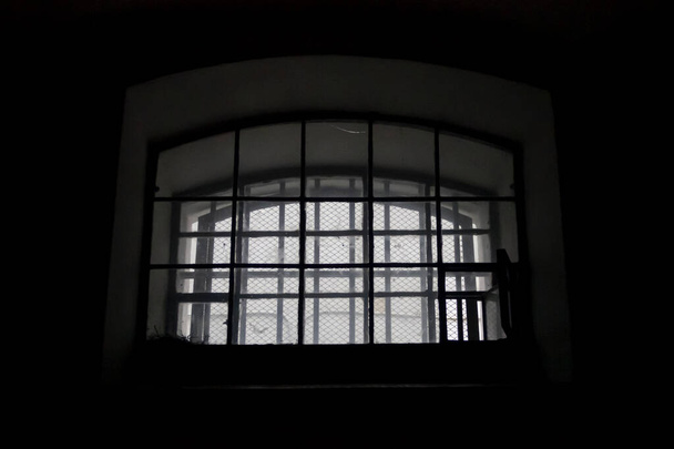 Ένα παράθυρο σε ένα κελί φυλακής, καλυμμένο με κάγκελα. Το εσωτερικό ενός παλιού σκοτεινού μοναχικού κελιού. - Φωτογραφία, εικόνα