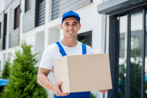 Young delivery man hold a cardboard box in his hands - Foto, Imagen