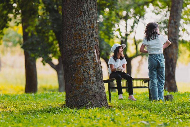 Close up photo of two girls outdoors, one girl posing standing with the back to the camera and another girl is sitting on a bench, resting after voluntary work for gathering garbage. - Foto, Bild