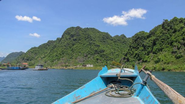 Olhando para o rio azul e alta montanha a partir do arco de um pequeno barco de madeira em Phong Nha - Ke Bang National Park, Ninh Binh Province, Vietnã - Foto, Imagem