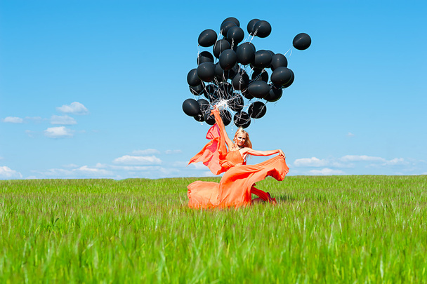 Woman in the orange dress with black balloons - Zdjęcie, obraz