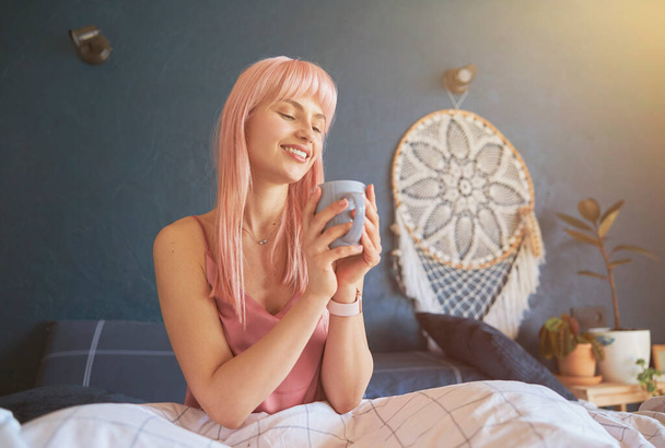 Pretty woman with pink hair holds mug sitting on comfortable bed with soft blanket - Photo, Image