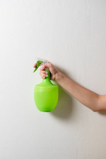 Bir kadının eli gri arka planda yeşil sprey şişeli plastik bir şişeyi tutuyor. Evde bakım ve temizlik kavramı. - Fotoğraf, Görsel
