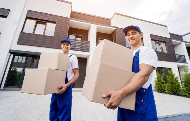 Two removal company workers unloading boxes into new customers home - Фото, изображение