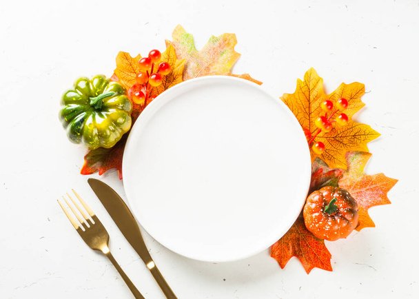 Herfsttafelopstelling met wit bord, gouden bestek en herfstdecoratie. - Foto, afbeelding