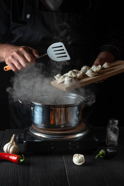 Professional chef cooks meat dumplings in a saucepan in the restaurant kitchen. Close-up of the hands of the cook during work. Free advertising space - Foto, afbeelding