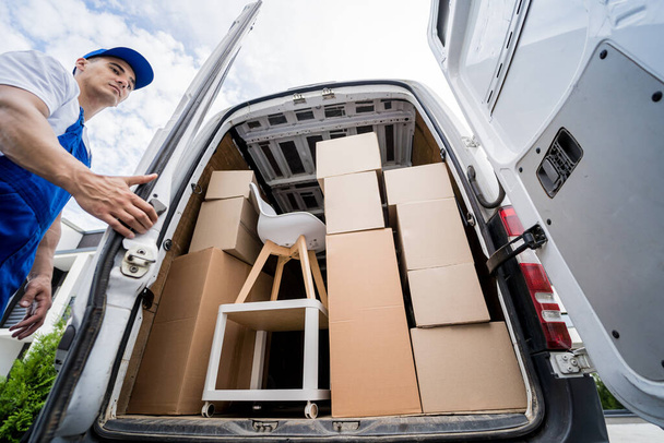 Two removal company workers unloading boxes and furniture from minibus - Fotoğraf, Görsel