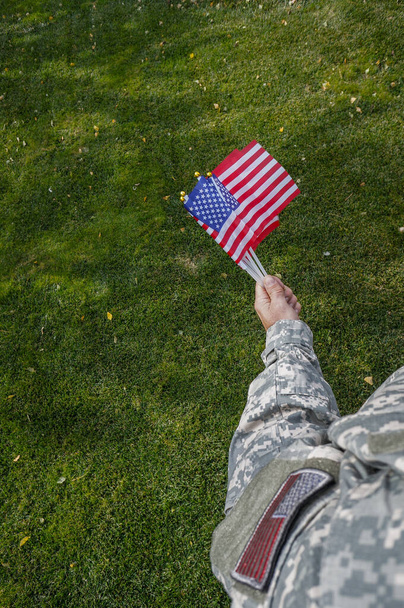 American soldier holding flags in his hand at the celebration over green grass in the park - Фото, изображение