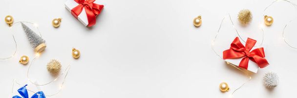 Urlaub winterrot. Weiße Geschenkschachtel mit roter Schleife, Neujahrskugeln und funkelnden Lichtergirlanden in weihnachtlicher Komposition auf weißem Hintergrund als Grußkarte. Festliche Dekoration, Kopierraum - Foto, Bild