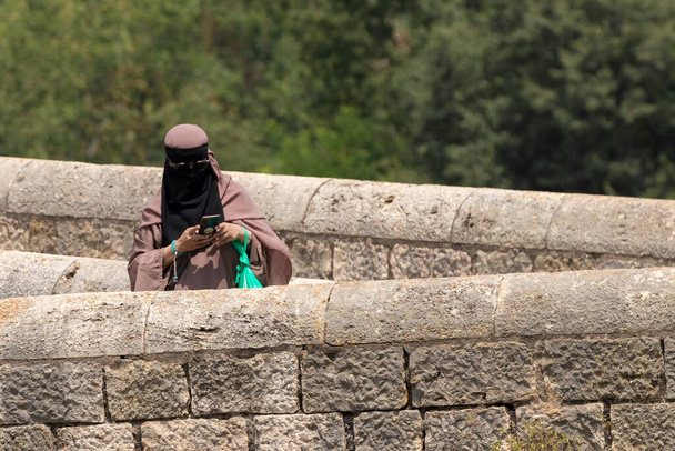 mujer en Burqa mirando a un móvil mientras cruza un puente de piedra - Foto, imagen