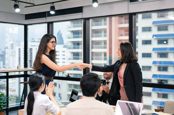 Многонациональная предпринимательница пожимает руку соглашению делового сотрудничества и поздравляет коллег в современном офисе - Фото, изображение