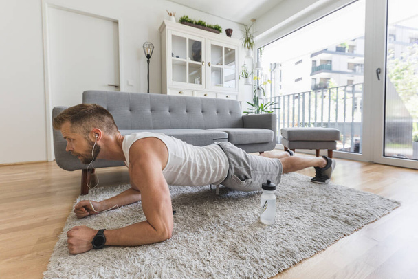 Handsome young man working out at home in the living room  - Фото, зображення