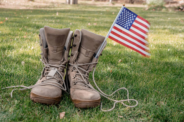 Boots of an American soldier who returned home as a symbol of a hero with an American flag waving in the wind - Valokuva, kuva