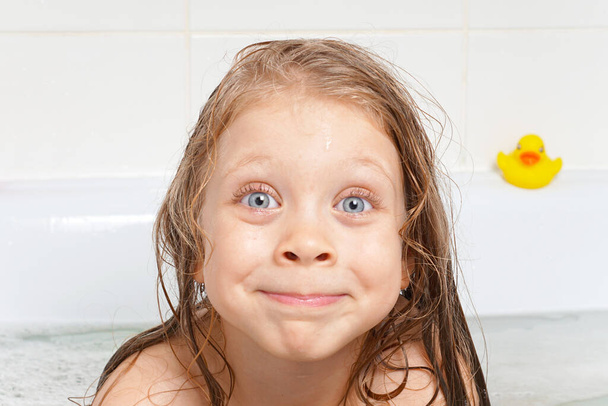 バスルームに長い髪のかわいい、美しい、陽気な女の子。シャボン玉で子供の感情。子供の衛生状態。水遊びだ。子供の衛生状態。健康 - 写真・画像