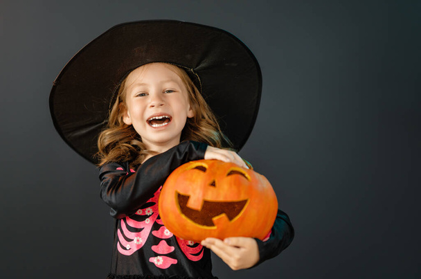 Happy Halloween! Cute little laughing girl in witch costume on black wall background.  - Φωτογραφία, εικόνα