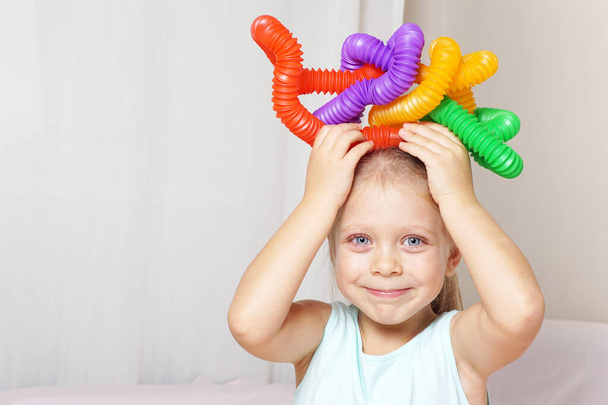 pop tube. anti-stress sensory plastic toy from a tube in the hands of a child. beautiful baby girl playing new modern toy pop tube. trend of 2021. A corrugated tube bent into an interesting metamorphosis shape. Toffee. - Fotó, kép