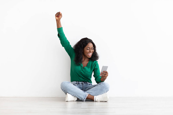 Emocional mujer negra jugando en línea, utilizando el teléfono celular - Foto, imagen