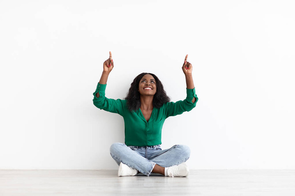 Jovem mulher negra alegre sentada no chão, mostrando espaço de cópia - Foto, Imagem